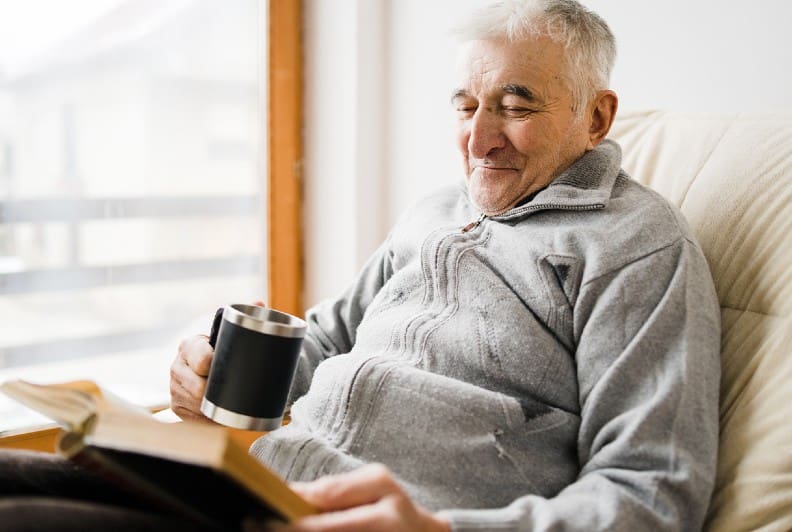 senior man drinks coffee and reads a book