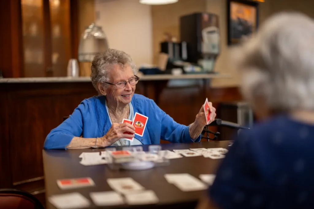 @ senior women playing a card game while discussing what is a life plan community like StoneRidge, also a CCRC in Mystic, CT.
