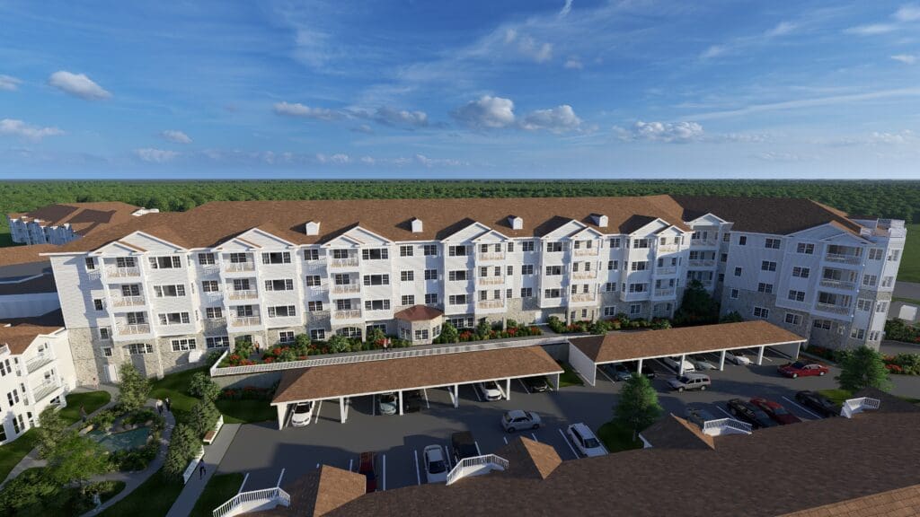 An aerial view of the West Elevation showcasing growth at StoneRidge in Mystic, CT. The image features a large white building with a brown roof for senior housing with other building and tree.