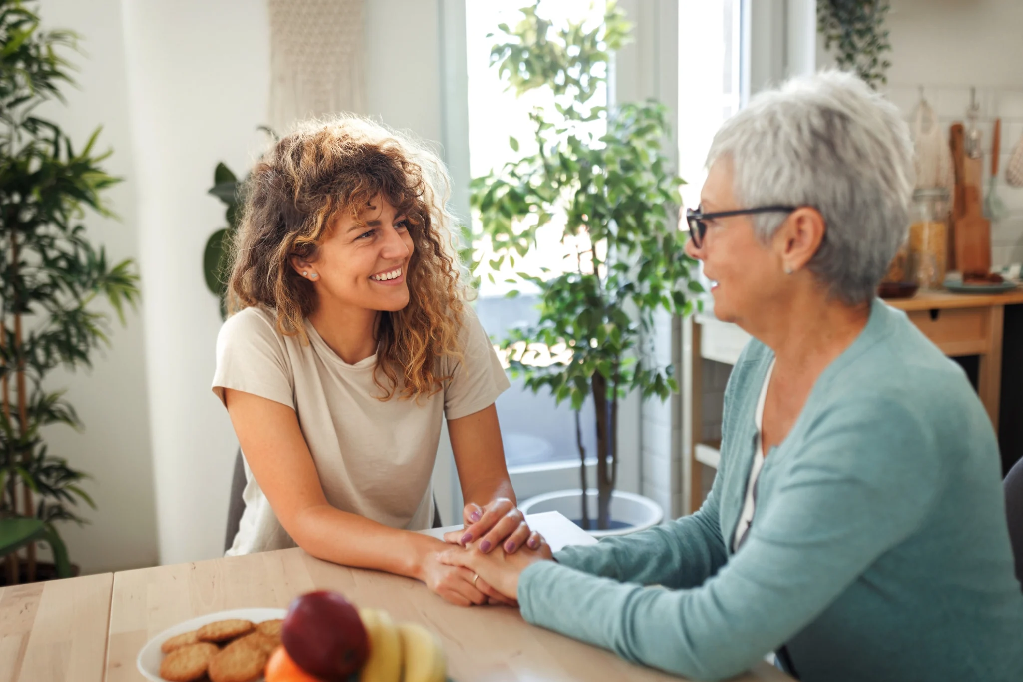 An adult woman holding her mother's hands while discussing how to find help for her aging parents and talking about independent living options at StoneRidge In Mystic, CT.