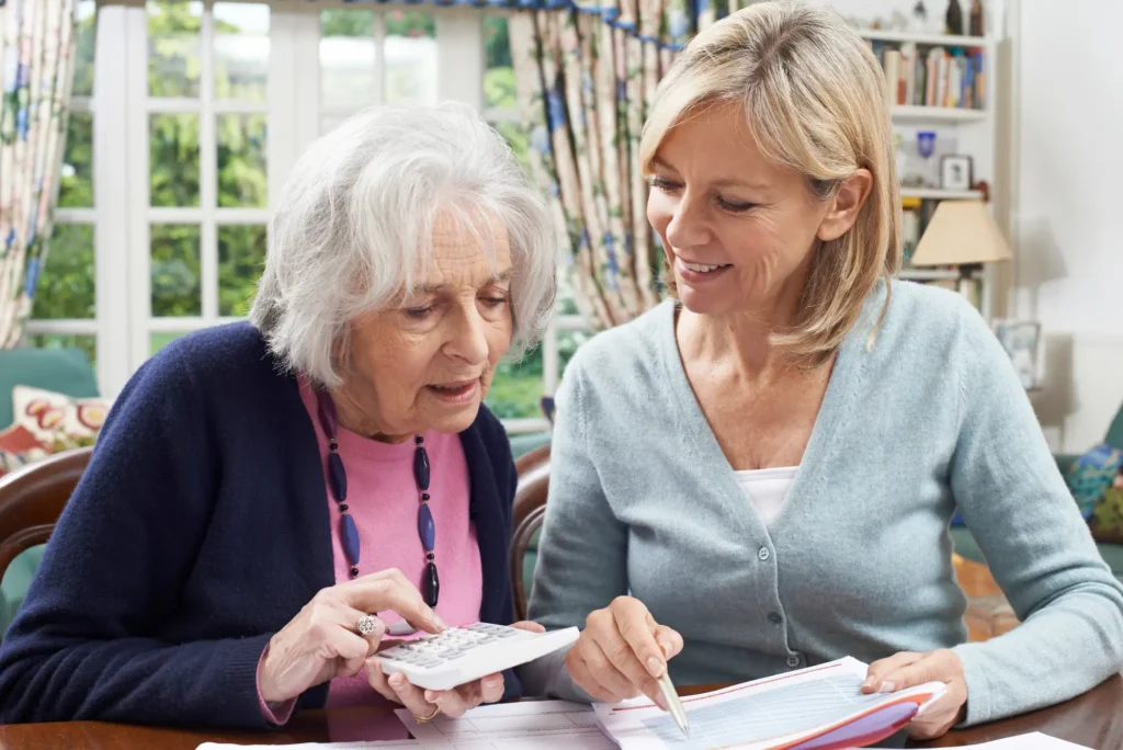 An elderly woman and her daughter using a calculator and discussing how senior living could be more cost-effective than homeownership.